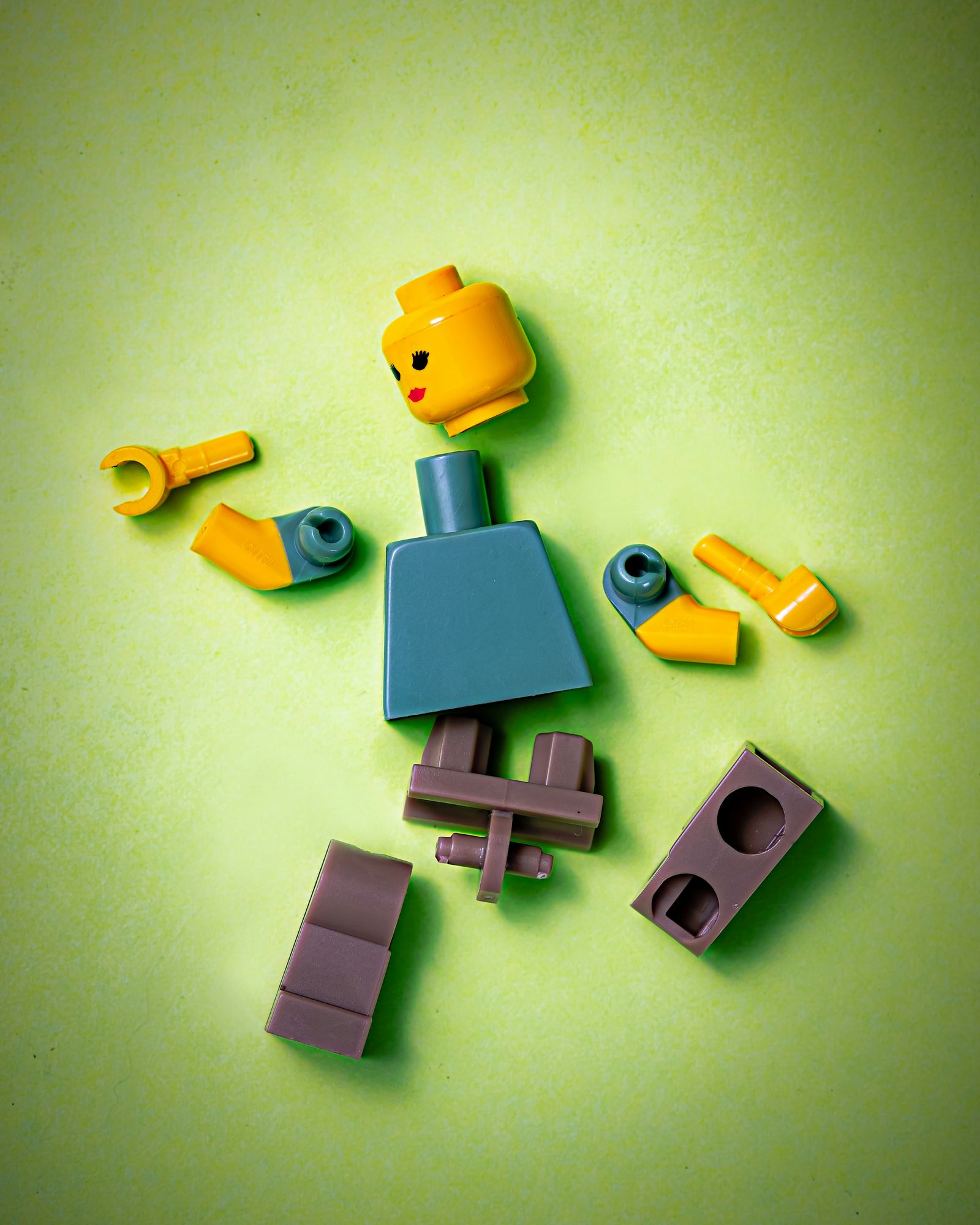 Die Einzelteile einer Lego-Figur liegen auseinandergenommen auf grünem Untergrund – abgesichert, wenn etwas zu Bruch geht