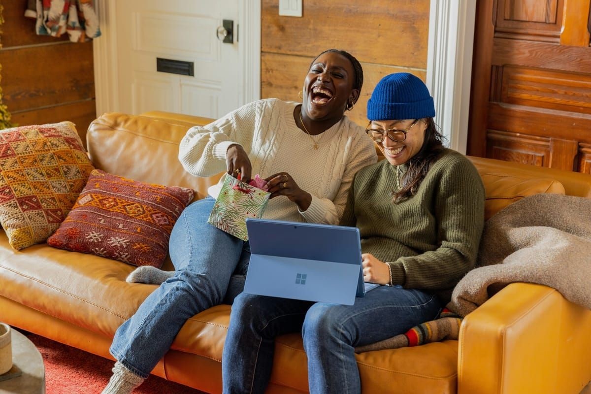 Zwei lachende Personen sitzen mit Laptop auf dem Sofa – gut abgesichert in jeder Lebenslage